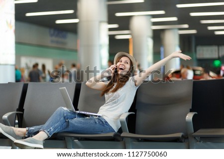 Joyful traveler tourist woman work on laptop talk on mobile phone call friend booking taxi hotel spread hands wait in lobby hall at airport. Passenger traveling abroad on weekend. Air flight concept