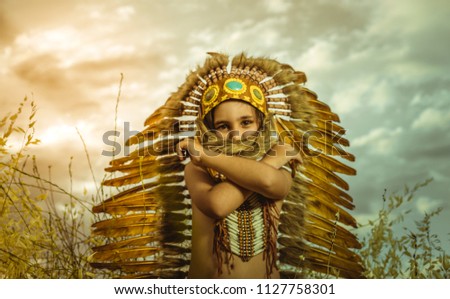 American Indian boy dressed in traditional feathered costume, wearing a tuft on his head, picture at sunset in a wheat field
