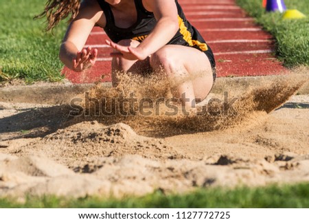Close up of a young female high school long and triple jumper landing violently in the sand during a competition. Royalty-Free Stock Photo #1127772725