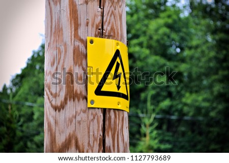 Electrical sign on a wooden post with blurry background.