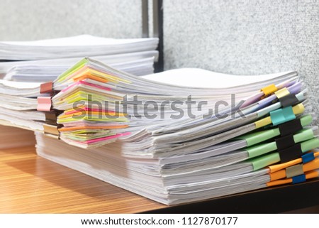 Close up pile of unfinished homework assignment separated by colorful paper clips on teacher's desk waiting to be managed and checked. Paperwork stacked in archive. Education and business concept.