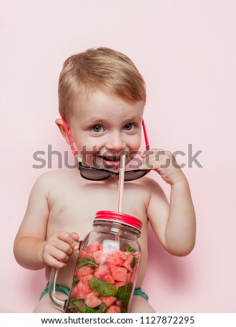 Little boy with Jar of cold fresh lemonade with piece of watermelon and ice on pink background.