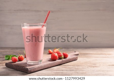 Glass with tasty strawberry smoothie on wooden table Royalty-Free Stock Photo #1127993429