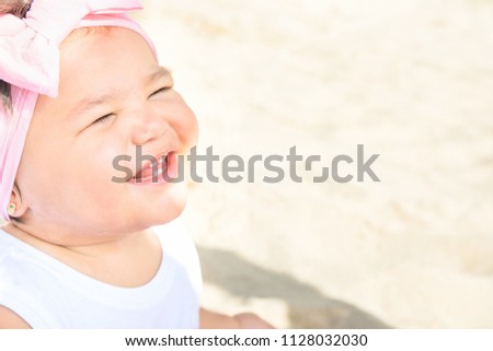 Cute Sweet 1 Year Old Baby Girl Toddler Sits on Beach Sand by Ocean Smiling. Sweet Face Expression. Bright Sunny Day. Parenting, Childhood Togetherness Family Joy. Poster with Copy Space