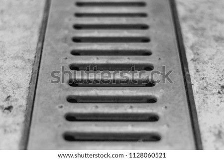 The drain for sewage is covered with steel grating. Black and white photo. Selective focus. 50 mm. Piece of pattern or background.
