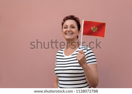 Montenegro flag. Woman holding flag of Montenegro. Nice portrait of middle aged lady 40 50 years old with a national flag over pink wall background. Visit Montenegro concept.
