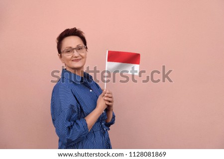 Monaco flag. Woman holding Monaco flag. Nice portrait of middle aged lady 40 50 years old with a national flag over pink wall background outdoors.