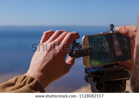 A man adjusts the smartphone on a tripod with lenses. The photographer travels taking pictures of the landscape using a mobile phone