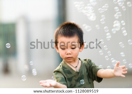 Asian boy in camo t-shirt playing with soap bubble outdoors
