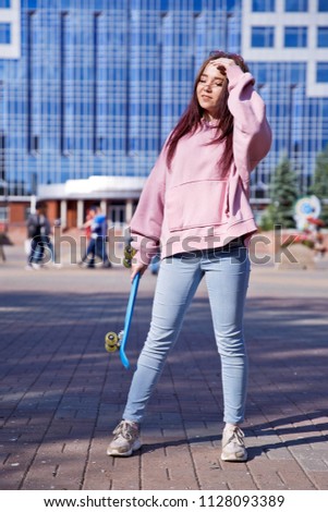 A beautiful girl with a skateboard in her hands is walking on a background of city skyscrapers.