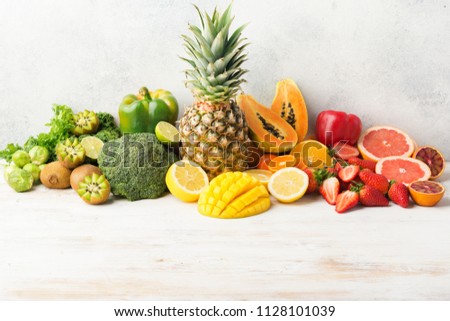 Vitamin C fruits and vegetables in rainbow colors, oranges mango grapefruit kiwi kale pepper pineapple lemon papaya broccoli, on white table, copy space for text in the bottom, selective focus