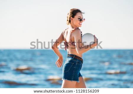beautiful happy young woman holding ball and running on beach