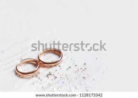 Golden wedding rings on paper invitation with shiny rhinestones. Wedding details, symbol of love and marriage. Place for text.