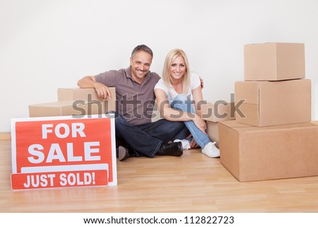 Happy family moving into the new home sitting in an empty room on the floor with small stack of cardboard boxes