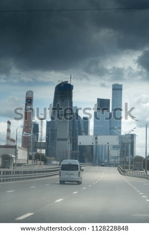 Asphalt road to the modern city. Dark stormy clouds.