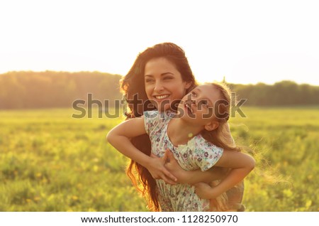 Happy enjoying mother hugging with her relaxing joying kid girl on sunset bright summer background. Closeup color portrait of love.