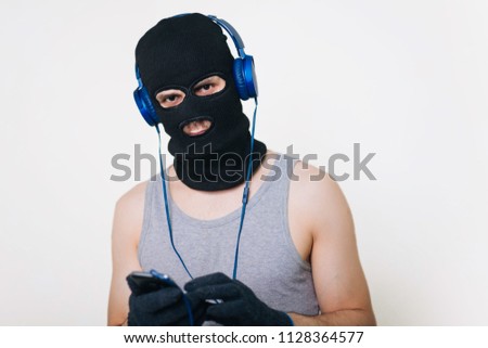 A man in a balaclava with a cell phone and headphones. the criminal downloads music is not legal. theft of music.