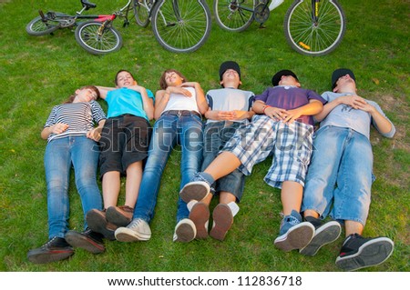 Teenage boys and girls lying in the grass after riding bicycles.