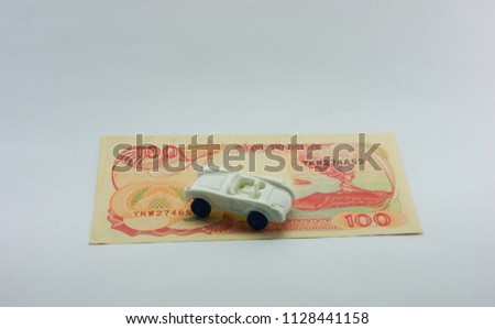 100 IDR old banknote and a plastic white car. concept of saving up money for dreams
