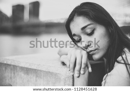 Latina woman leaning on concrete piller in front of Ohio River and Roebling Bridge with eyes closed in black and white