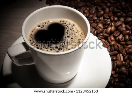 white cup of coffee with a picture of a heart on a background of roasted coffee beans close up