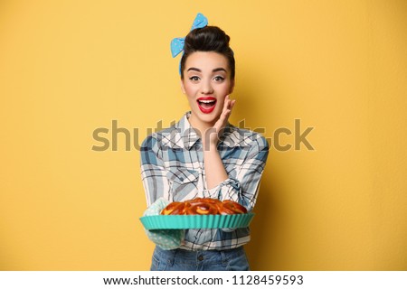 Funny young housewife with homemade pastry on color background Royalty-Free Stock Photo #1128459593