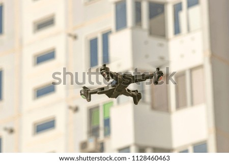 Flying drone quadcopter in front of white multi-storey building.
