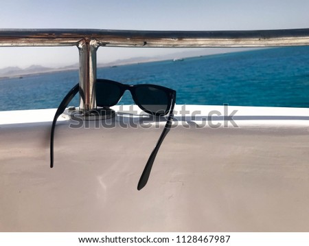 Black protective sun-protective plastic glasses hang on beryl aboard a tourist vessel, yacht and sailboat, boat, liner at the resort, the sea, on a tropical blue sky background.