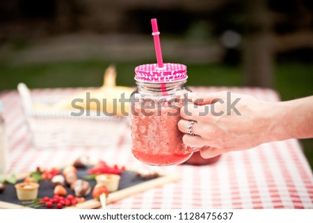 woman holding strawberry fresh in mason jar, sweets, cupcakes,  lemonade,  fresh, bananas,  red currant on red checkered tablecloth in the background - healthy summer snacks and drinks