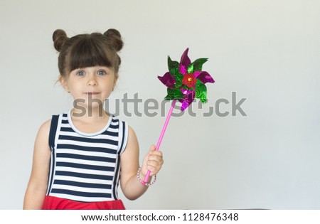Cute little girl holding colorful toy pinwheel on grey background. Copy space for advertising