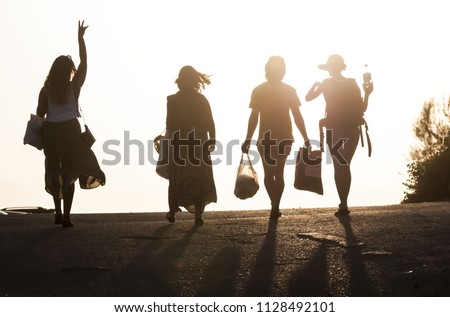 Silhouettes of four best friends walking in the sunset. One girl raises her hand. Four people silhouette against the sundown as they walk and converse. Set for the picnic. Three girls and one boy.