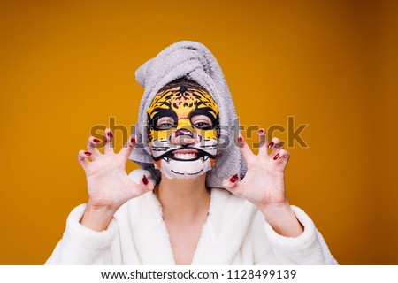 a funny young girl in a bathrobe and with a towel on her head growls like a beast, on her face moisturizing with a picture of the muzzle of a leopard