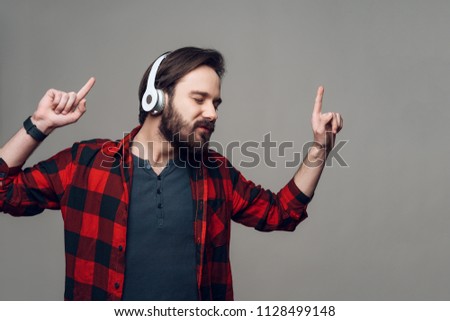 Happy Guy Listening to Music with Headphones. Handsome Smiling Guy in Checkered Shirt with Closed Eyes dancing with headphones. Isolated on Gray Background. Concept of People Emotions