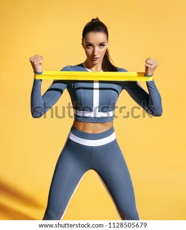Sportswoman performs exercises for the muscles of the hands. Photo of woman workout with resistance band on yellow background. Strength and motivation.