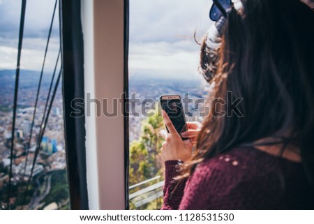 Woman taking pictures of a city with her smartphone from the inside of a funicular