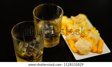 glass of whiskey with ice cubes and salty snacks on a black background, party time