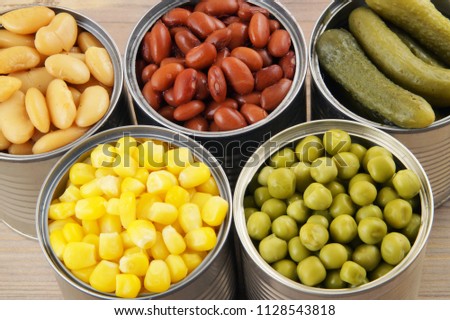 Openned tin cans with different food. Green peas, sweet corn, cucumbers and beans on wooden background.