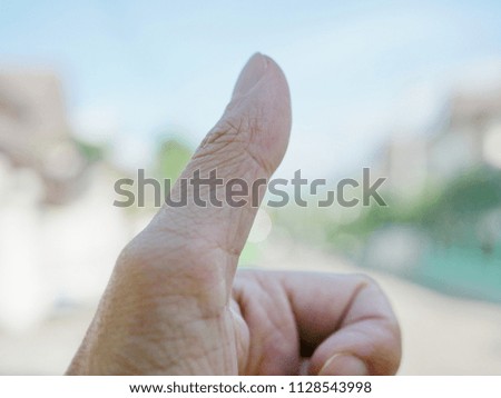 Closeup of a thumb doing a thumbs-up gesture on a light defocus background representing approval and satisfaction