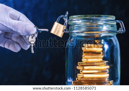 Hand in glove with key, Jar bank with security lock and a gold bars inside on black background. Protection deposit concept.Keeping money for the future. Royalty-Free Stock Photo #1128585071