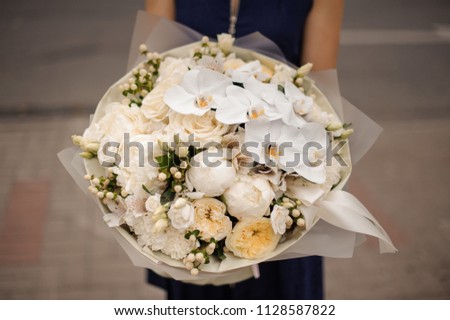 Girl in the blue dress holding in her hands a beautiful bouquet of white orchids and champagne color peonies and roses in the gift paper