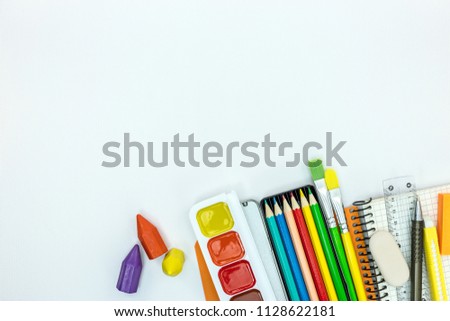 school stationary and tools for kids. notebook, paint, pencils on white desk surface, flat view