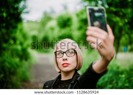Beautiful urban woman taking picture of herself, selfie. Girl on green park background with blurred background