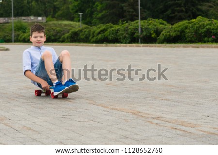 on a walk in the park a boy sits on a skateboard and rides