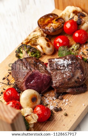 Two juicy steaks with roast medium rare, with grilled vegetables on a wooden board. Cooked with air fryers. A laid table in the restaurant for a holiday or birthday, evening dinner. selective focus