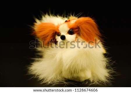 Very small toy souvenir, dog, bird feather dog on black background, isolated, white with brown ears.