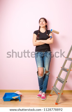 Image of young woman with paint roller standing near staircase