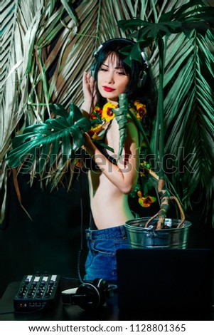 Brunette girl in bikini on tropical leaves background enjoys music on headphones . DJ woman plays music disko party on the equipment in the summer club.