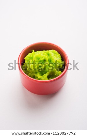 Green wasabi sauce or paste in bowl, with chopsticks or spoon over plain colourful background. selective focus
