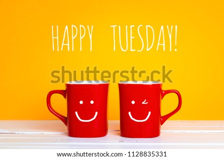 Two red coffee mugs with a smiling faces on a yellow background with phrase Happy tuesday. Happy coffee mugs. Royalty-Free Stock Photo #1128835331