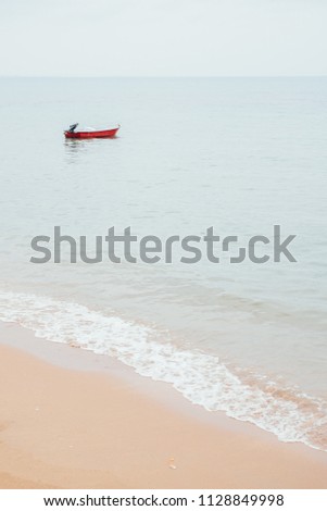 A lonely red boat in the sea with soft waves on sandy beach